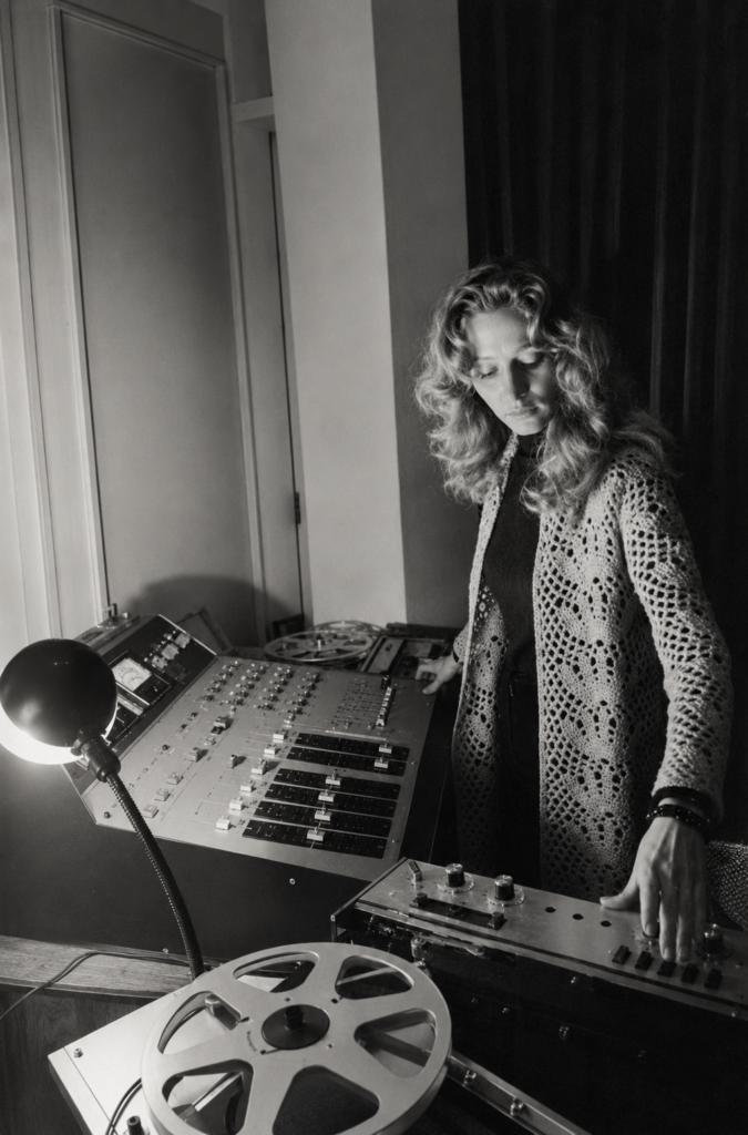 Fotografía en blanco y negro de la compositora francesa Éliane Radigue operando una consola de mezcla de audio analógica y magnetófonos de bobina abierta en su estudio.