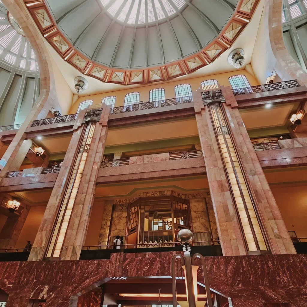 Vista interior de la cúpula y los niveles del Palacio de Bellas Artes, mostrando la fusión de mármol y detalles de herrería Art Nouveau en la Ciudad de México.