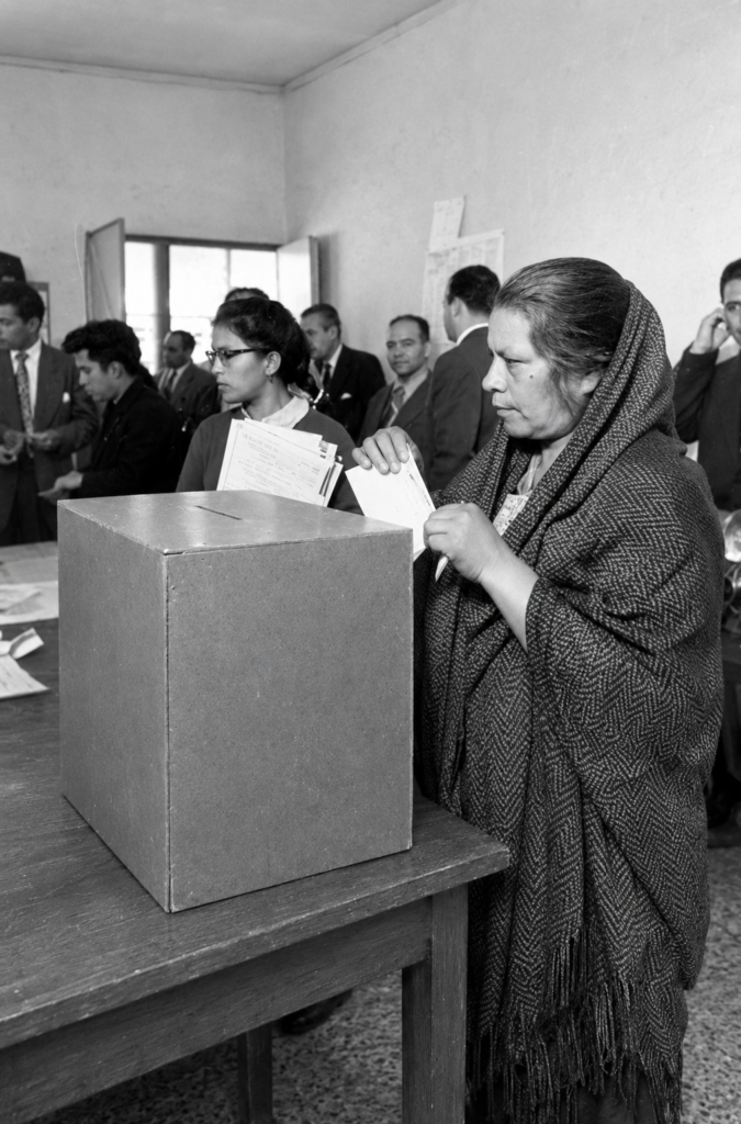 Fotografía histórica en blanco y negro de una mujer mexicana con rebozo introduciendo su boleta en una urna electoral de madera durante las elecciones del 3 de julio de 1955 en México.