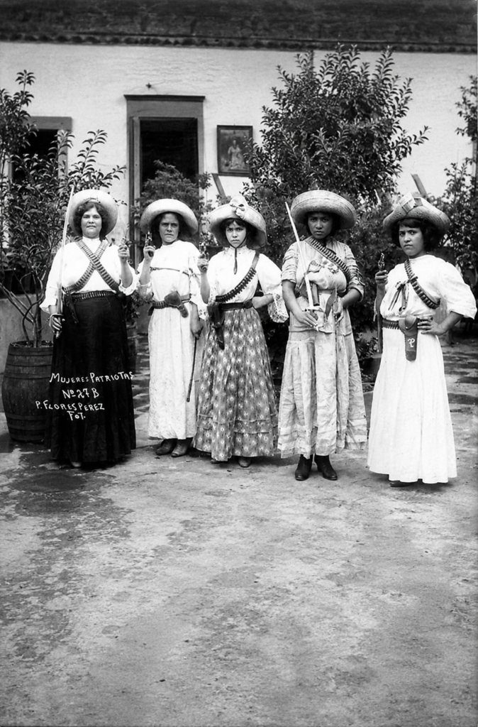 Fotografía histórica de cinco mujeres revolucionarias mexicanas o soldaderas zapatistas posando con armas, sables y carrilleras, capturada por P. Flores Pérez en México. Imagen ideal para ilustrar poemas y literatura de la Revolución Mexicana.