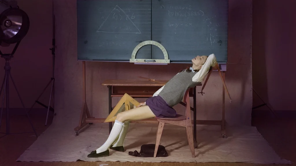 Escena de la película Nymphomaniac de Lars von Trier con Stacy Martin en un salón de clases frente a un pizarrón con fórmulas matemáticas.