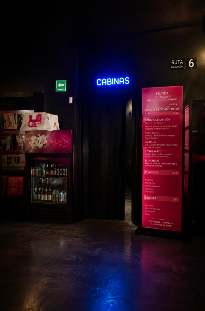 Entrada a cabinas sexuales con letrero de neón azul y menú de bebidas alcohólicas en una sex shop de la CDMX.