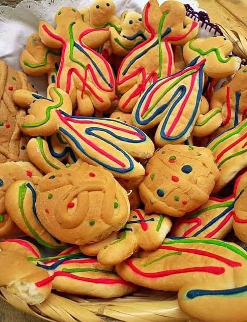 Pan de muerto mikapantsi con figuras humanas y piezas redondas, decorado con líneas rojas, verdes y azules en una canasta.
