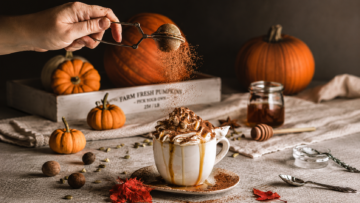 Pumpkin Spice: Receta de la bebida de calabaza de Starbucks Una taza de café con leche sobre una mesa de madera rústica, decorada con espuma, una pizca de canela y hojas de otoño alrededor, ilustrando la receta de Pumpkin Spice Latte