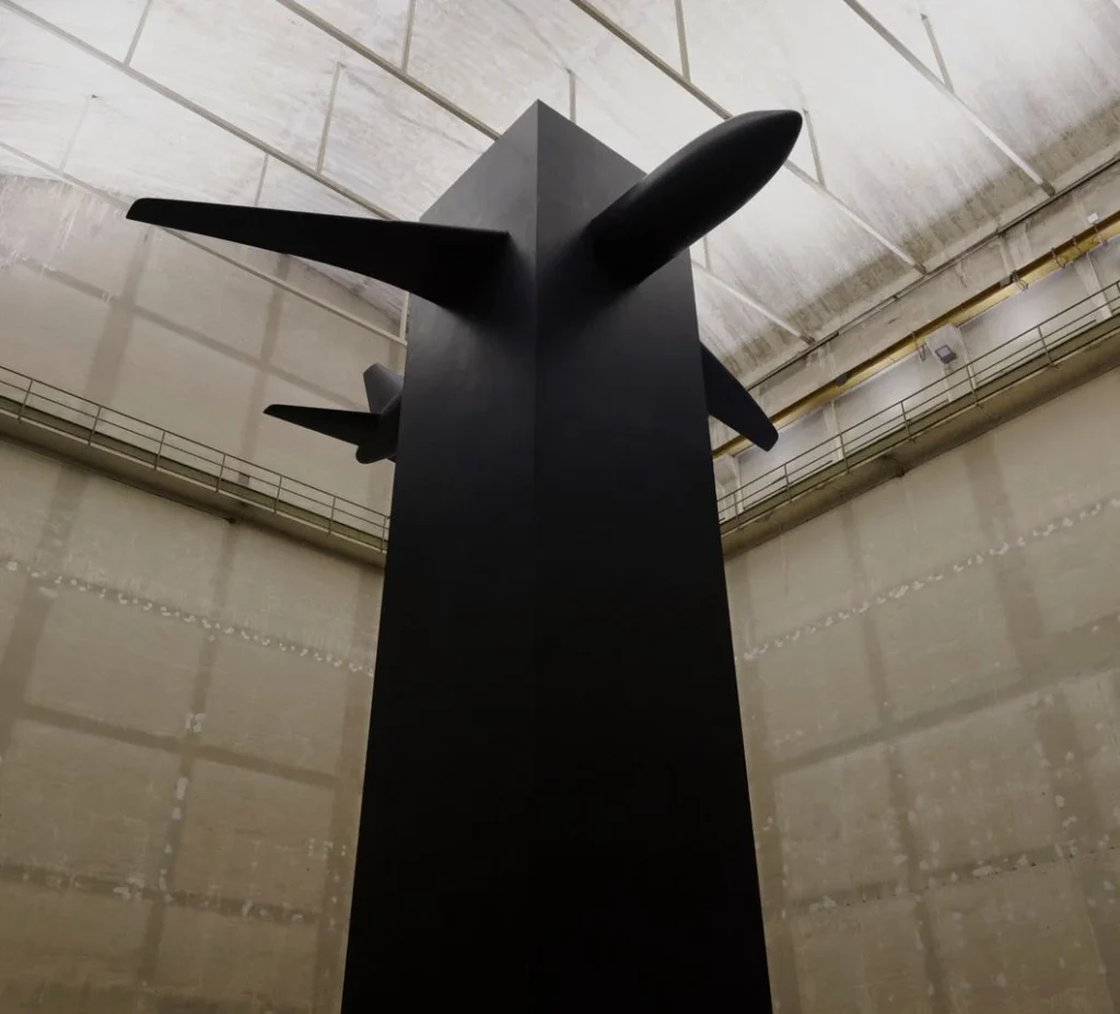 Instalación de la obra Blind de Maurizio Cattelan en el Pirelli HangarBicocca, que muestra un enorme monolito negro de resina atravesado por la silueta de un avión.