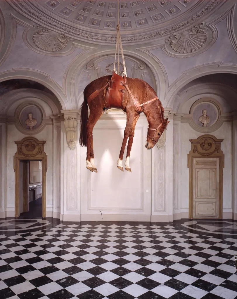 Instalación de la obra Novecento de Maurizio Cattelan que muestra un caballo taxidermizado suspendido del techo en un palacio barroco.