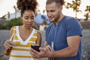 two-friends-with-beer-bottles-looking-at-cell-phon-2024-09-15-14-07-49-utc