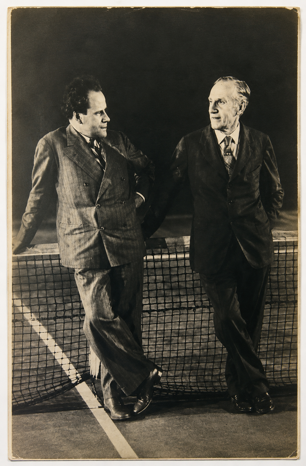 Fotografía en blanco y negro del escritor estadounidense Upton Sinclair y el cineasta soviético Serguéi Eisenstein conversando junto a una red de tenis en California.