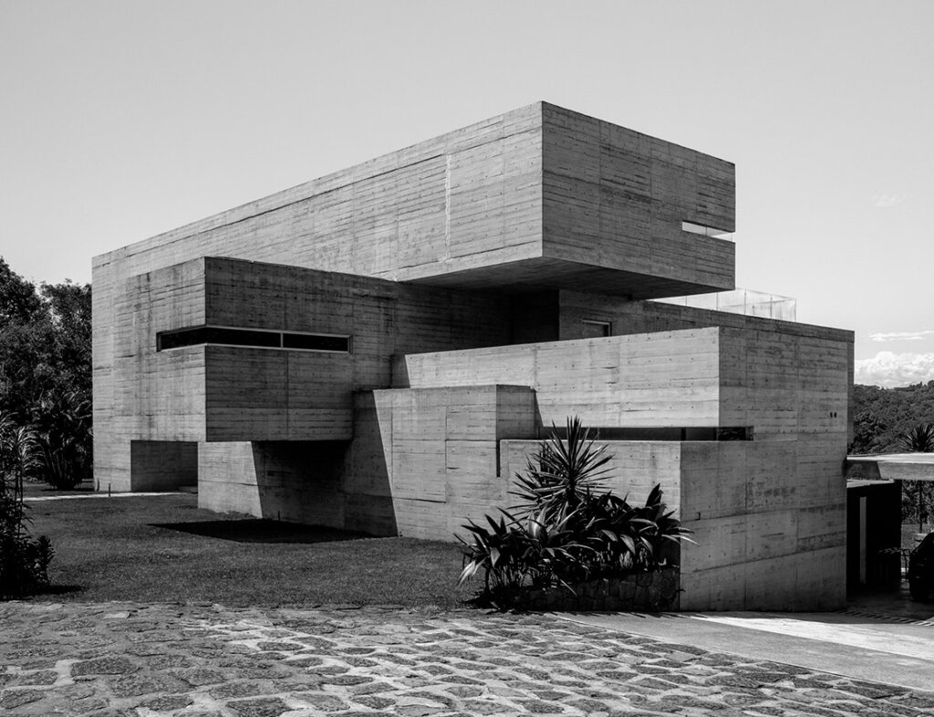 Fotografía en blanco y negro de la fachada posterior de la Casa Oyamel en Xalapa, Veracruz, destacando su composición geométrica de volúmenes apilados y desfasados de concreto crudo expuesto.