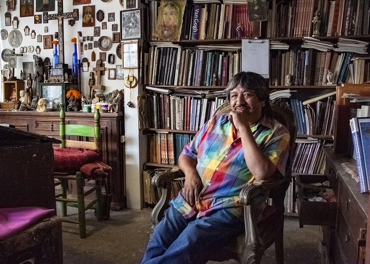 Retrato de Alfredo Vilchis, el Da Vilchis de la Lagunilla, sentado en su estudio rodeado de exvotos y herramientas de pintura. Fotografía original de Mariela Santoni para Yaconic.