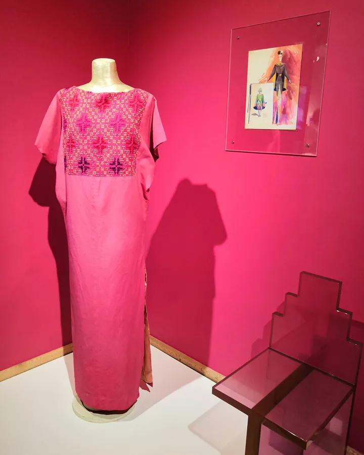 Vestido largo tipo huipil color rosa mexicano con bordado indígena tradicional expuesto en un museo junto a un boceto de moda original de Ramón Valdiosera.