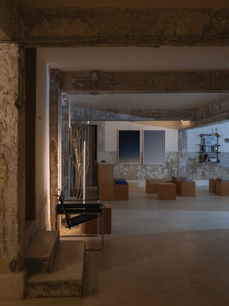 Interior de diseño industrial y minimalista de Sona Listening Space en la Condesa, CDMX, con pilares de concreto expuesto, asientos geométricos de madera y cuadros abstractos.