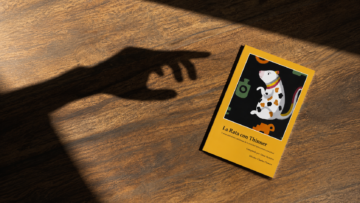 Edición física del libro La Rata con Thinner y otras anécdotas cotidianas de la sociedad latinoamericana sobre una mesa de madera con una sombra de mano.