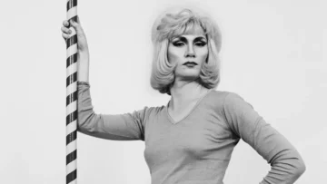 Retrato en blanco y negro de Jayne County, pionera trans del proto-punk, posando con elegancia frente a una columna rayada durante los años setenta.