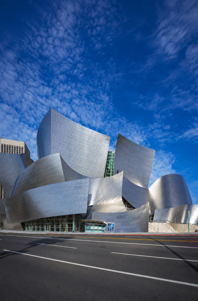 Vista exterior en ángulo contrapicado del Walt Disney Concert Hall en Los Ángeles, mostrando la fachada fluida de paneles de acero inoxidable y formas deconstructivistas diseñada por el arquitecto Frank Gehry bajo un cielo azul con nubes.