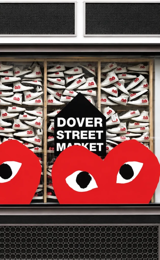 Escaparate de Dover Street Market exhibiendo una instalación masiva de calzado Comme des Garçons Play. El diseño integra el logotipo icónico del corazón rojo con ojos en una concept store que combina alta moda y cultura urbana bajo el concepto de 'Beautiful Chaos'.