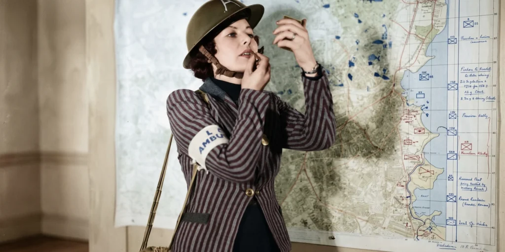 Una voluntaria de ambulancia británica se aplica lápiz labial rojo intenso ante un mapa de operaciones durante la Segunda Guerra Mundial, representando el 'Victory Red' como un símbolo de resistencia patriótica y desobediencia civil frente al fascismo