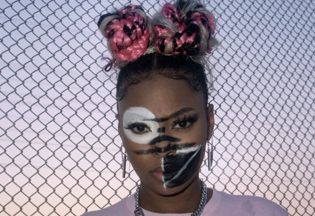 Una mujer con peinado de moños trenzados y maquillaje facial asimétrico en blanco y negro, diseñado específicamente para confundir los algoritmos de reconocimiento facial mediante la técnica CV Dazzle de camuflaje algorítmico.