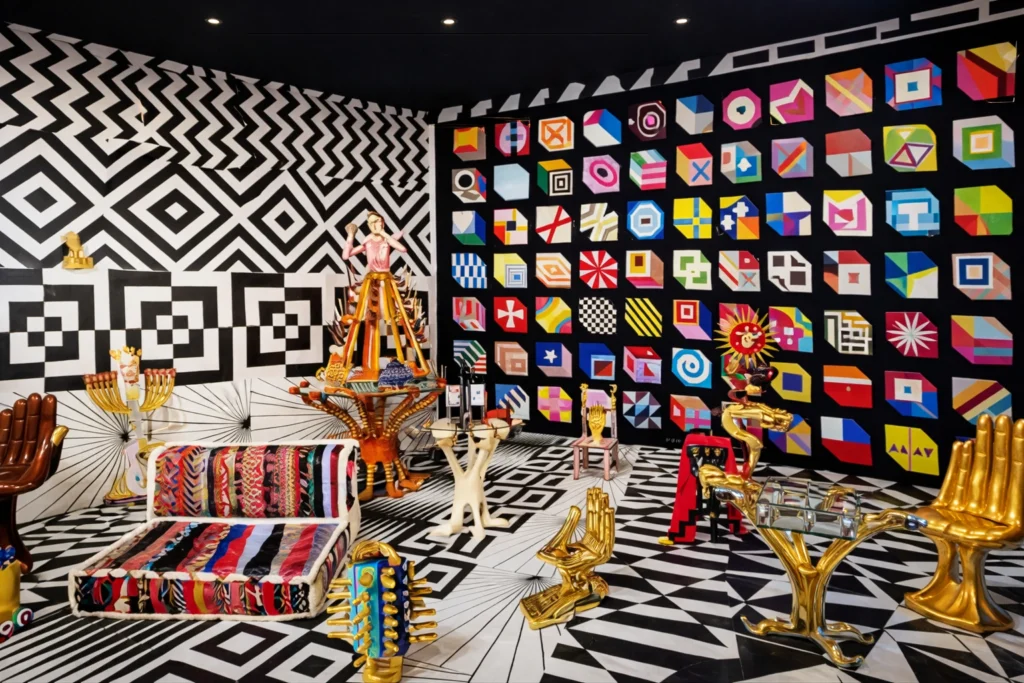 Exhibición de mobiliario y muros intervenidos por Pedro Friedeberg con la icónica silla mano dorada en primer plano.