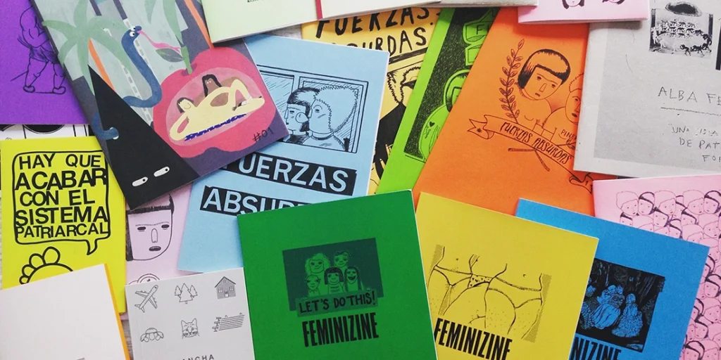 Variedad de fanzines contemporáneos y publicaciones independientes de colores vibrantes sobre una mesa, mostrando portadas con ilustraciones, tipografía experimental y temáticas feministas y de autogestión.