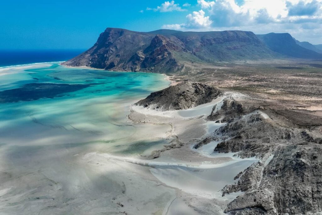 Vista aérea de la laguna de Detwah en la isla de Socotra Yemen con arena blanca y agua turquesa junto a montañas áridas.