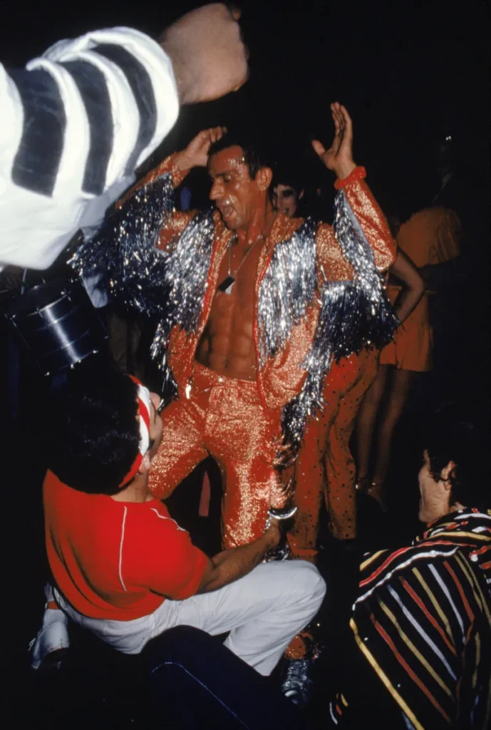 Un hombre con traje de lentejuelas brillantes bailando en la pista de Studio 54, capturando la energía frenética y la libertad estética de la era disco.
