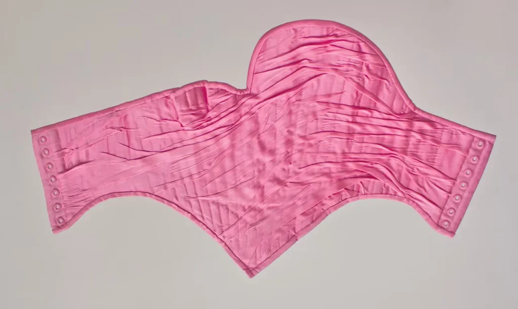 Plano detalle de un corsé rosa diseñado por Michaela Stark, mostrando los pliegues de seda y la estructura técnica de la prenda sobre un fondo neutro.