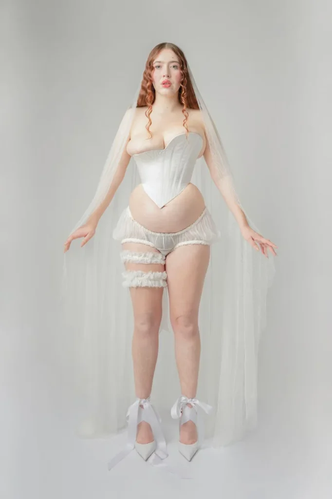 Michaela Stark vestida de novia con corsé blanco y velo, explorando la estética nupcial y la deformación corporal artística.