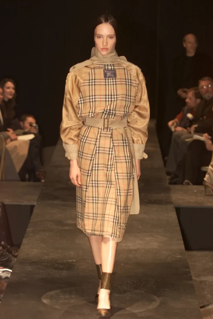 Modelo en pasarela luciendo el icónico abrigo de Burberry invertido diseñado por Miguel Adrover para su colección Fall 2000, un hito del upcycling y la crítica a las marcas de lujo.