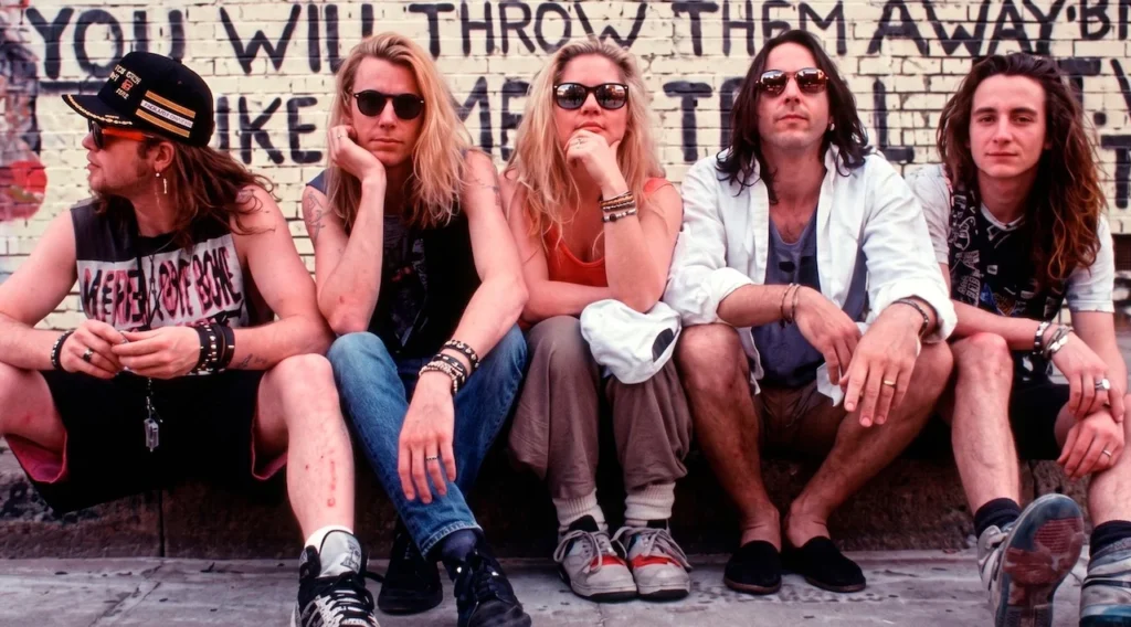 Los integrantes de la banda Mother Love Bone, incluyendo a Jeff Ament y Stone Gossard, sentados frente a una pared de ladrillos con graffiti en Seattle, mostrando la estética grunge de principios de los 90.