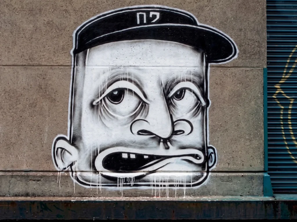 Grafiti de un rostro estilizado de Barry McGee (Twist) con ojos lánguidos y goteo de pintura, representativo de su estética de la Mission School.