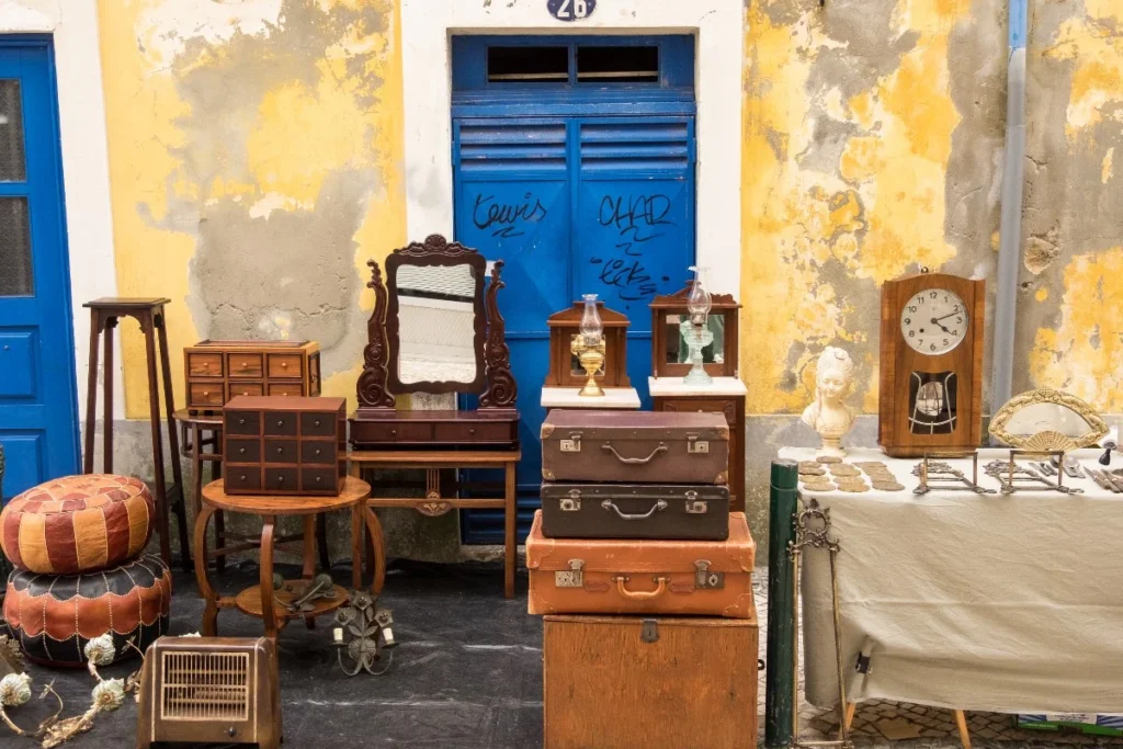 Antigüedades y muebles antiguos de madera con maletas vintage, un reloj de pared y candelabros en un bazar de la CDMX.
