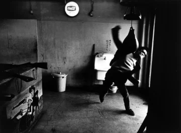 Revista Provoke: qué fue y por qué cambió la fotografía japonesa Fotografía urbana en blanco y negro de Shōmei Tōmatsu de 1966 que muestra a un boxeador entrenando dinámicamente con un saco de boxeo en un gimnasio subterráneo de Shinjuku, Tokio, con un letrero de Coca-Cola al fondo.