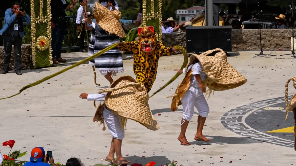 Danzante con traje y máscara de jaguar saltando junto a personajes con sombreros grandes de paja en la Danza de los Tecuanes.
