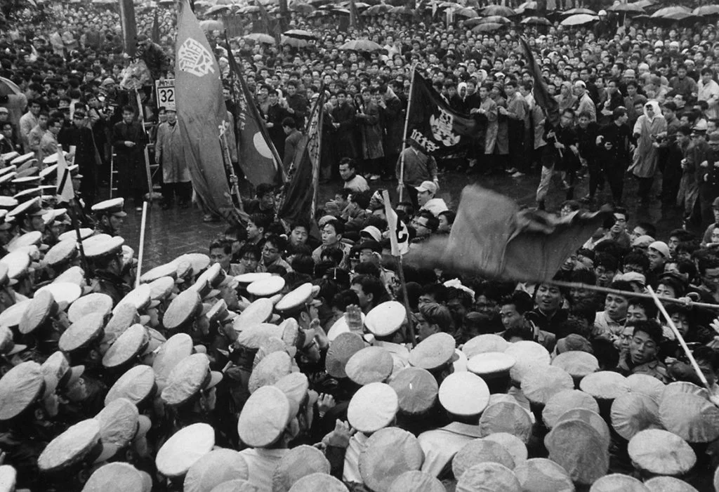 Fotografía en blanco y negro de Hiroshi Hamaya que muestra un choque masivo entre una multitud de policías con gorras blancas y estudiantes manifestantes de la organización Zengakuren con banderas ondeando en Tokio, durante las protestas de ANPO en 1960.