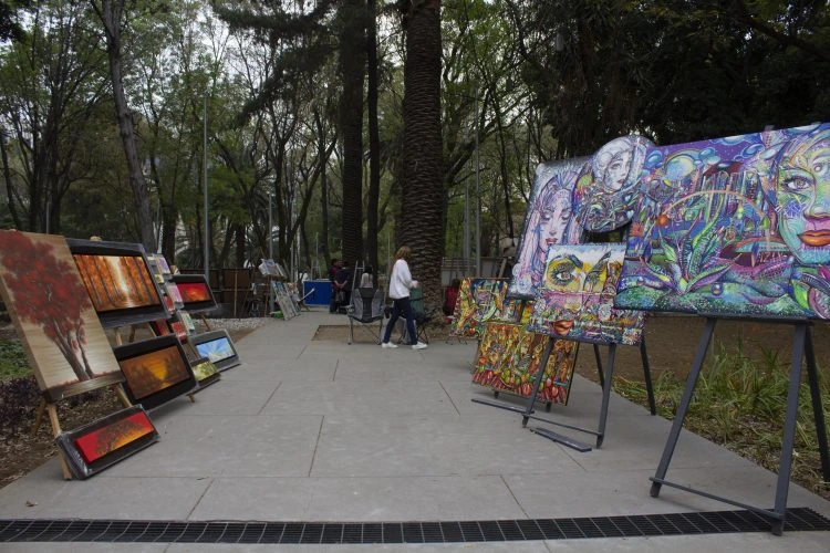 Cuadros y pinturas al óleo expuestos en caballetes en el andador peatonal del Jardín del Arte Sullivan en la CDMX.