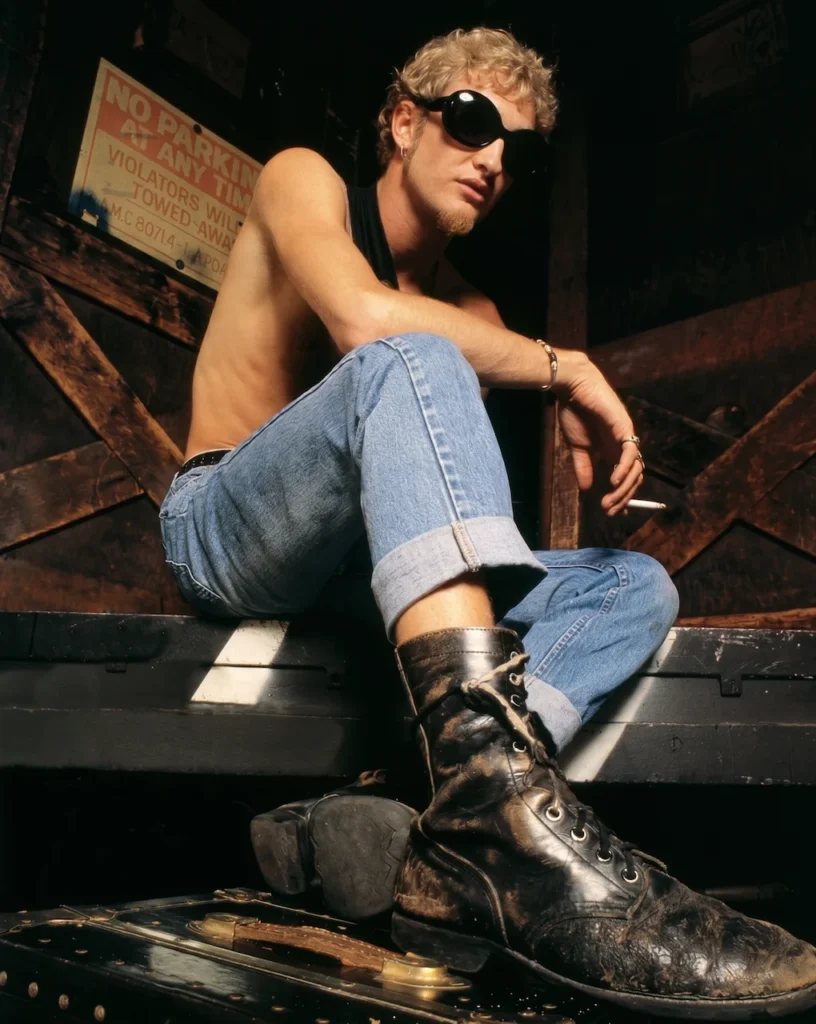 Layne Staley, vocalista de Alice in Chains, posando con gafas oscuras, jeans con dobladillo y botas industriales Dr. Martens en un entorno industrial durante la era de la película Singles.
