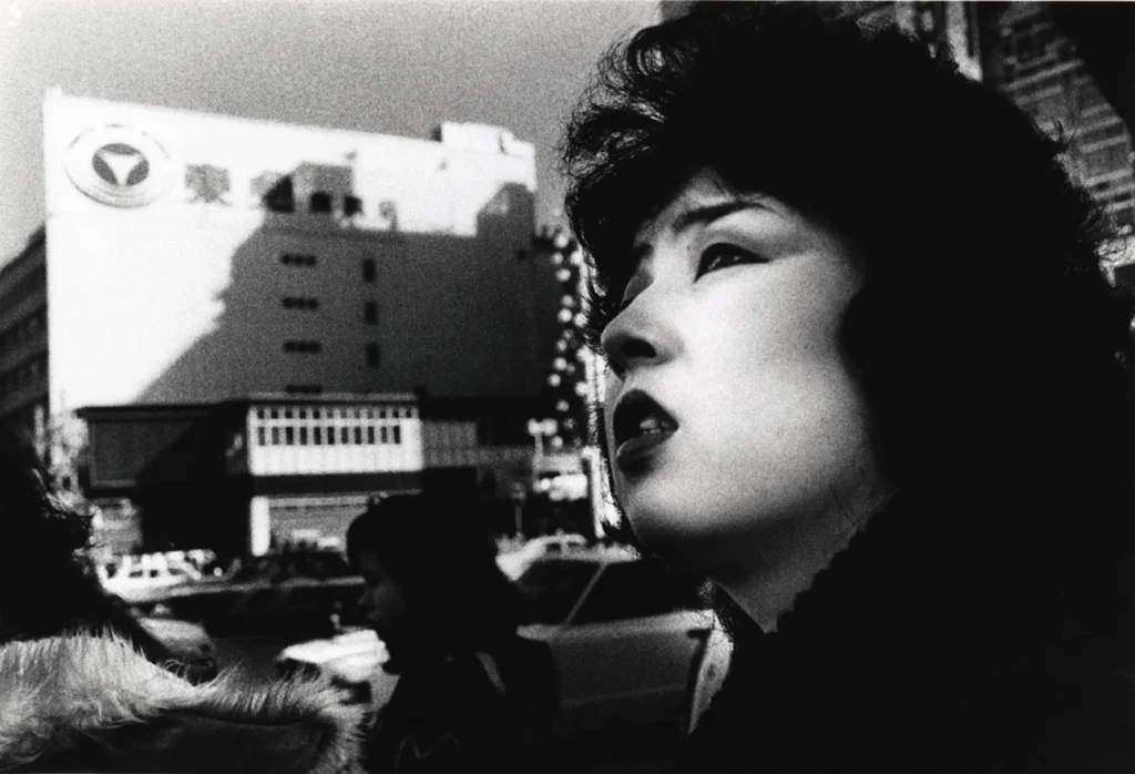 Fotografía callejera en blanco y negro de Daido Moriyama que muestra el perfil de una mujer japonesa con alto contraste y grano cinematográfico en una calle de Shinjuku, Tokio.
