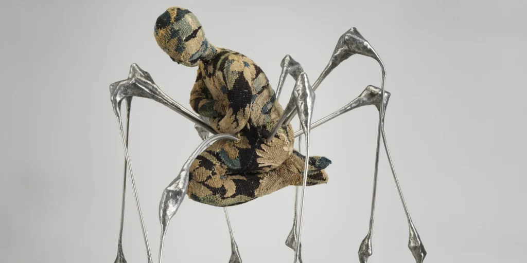 Escultura de Louise Bourgeois que fusiona una figura humana tejida con extremidades arácnidas metálicas, representando la fragilidad y la protección del trauma infantil.