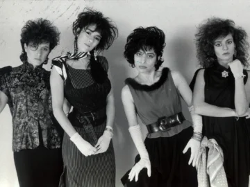 Bandas de mujeres en el rock latinoamericano: punk, metal y escenas underground Fotografía en blanco y negro de las cuatro integrantes de la banda argentina Viuda e Hijas de Roque Enroll en los años 80. De izquierda a derecha: María Gabriela Epumer con camisa estampada; Mavi Díaz con vestido a rayas y pañuelo; Claudia Ruffinatti con blusa de cuello de piel y guantes blancos; y Claudia Sinesi con vestido oscuro. Posan mirando a la cámara con peinados altos y batidos estilo de la época.