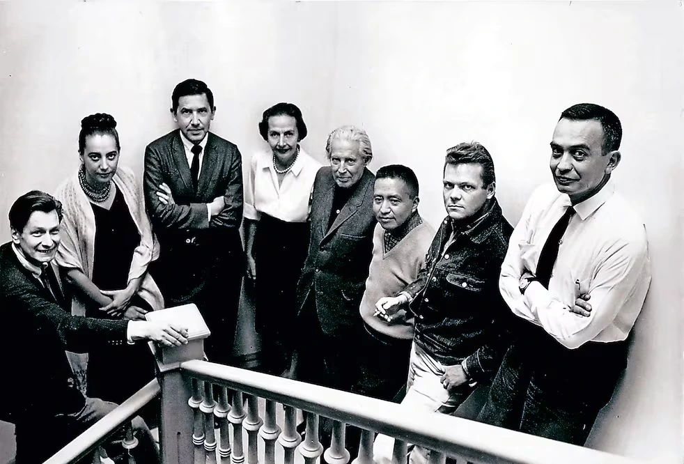 Fotografía en blanco y negro de Inés Amor junto a Leonora Carrington, Gunther Gerzso y otros artistas masculinos posando alineados en una escalera interior.