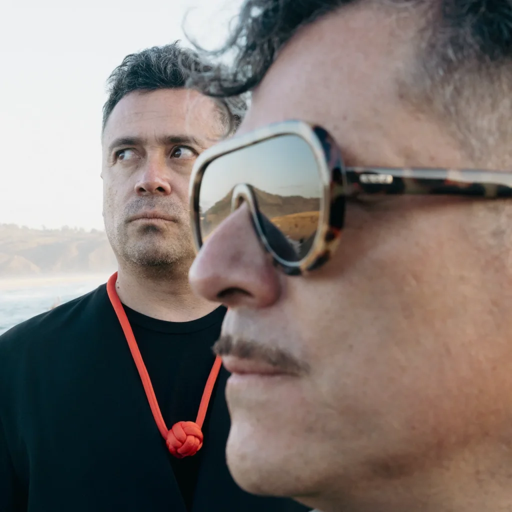 Primer plano de perfil de Felipe Ilabaca con lentes de sol y Pablo Ilabaca al fondo en sesión fotográfica para su sencillo Señorita.