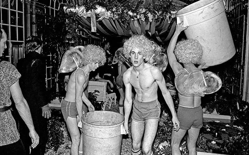Meseros o busboys disfrazados de cupidos con pelucas y alas cargando botes de basura en el club Studio 54 de Nueva York, década de 1970.