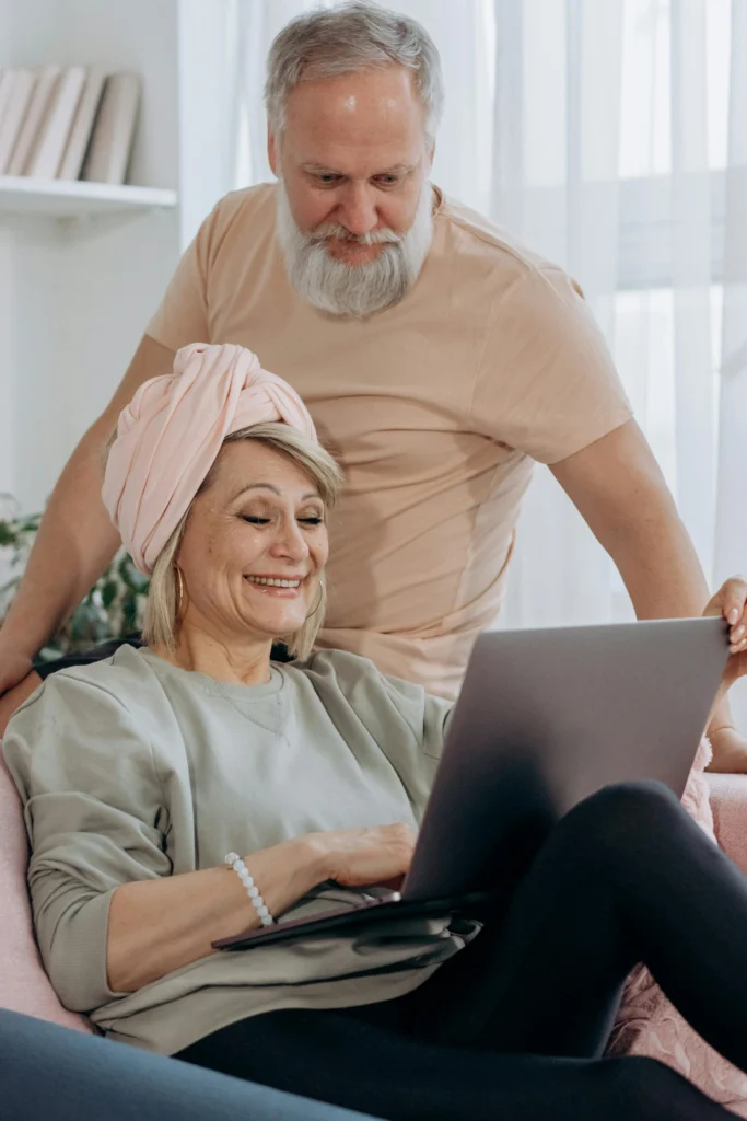 Pareja de adultos mayores sonriendo mientras miran una computadora portátil en la sala.