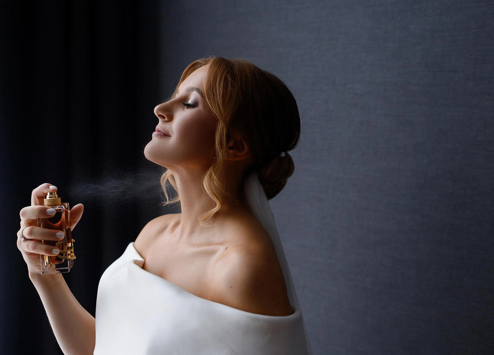 Mujer pelirroja vestida de novia aplicándose el perfume de lujo Yves Saint Laurent Libre en el cuello durante su preparación antes de la boda.