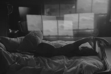 Cuentos cortos eróticos: cinco relatos breves sobre deseo Fotografía artística en blanco y negro de una mujer recostada en una cama deshecha frente a la ventana, ideal para cuentos eróticos breves.