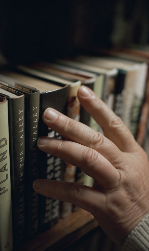 Mano seleccionando un libro de lomo oscuro en un estante de madera.
