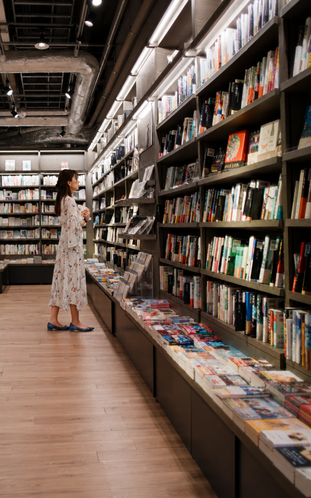Mujer con vestido blanco mirando estanterías llenas de libros en una librería moderna.