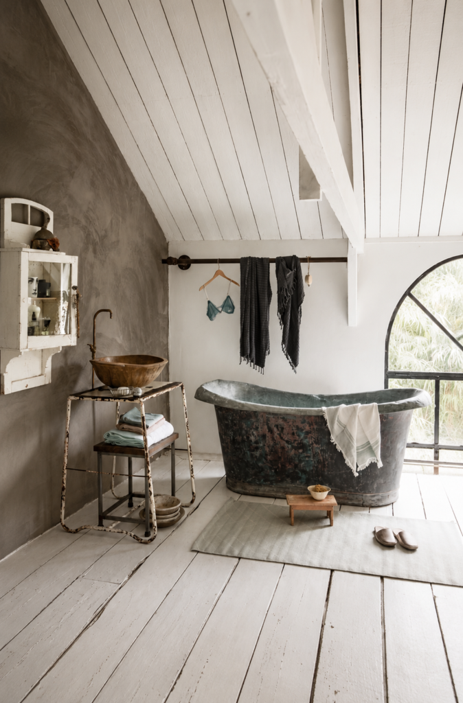 Diseño de baño estilo wabi sabi en un ático con suelo de tablones de madera blanca gastada, una bañera exenta de zinc envejecido, paredes de cemento pulido gris y un lavabo de madera rústica.