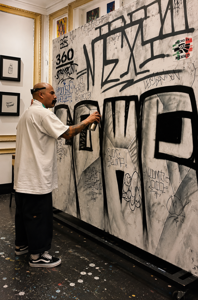 Marco Osorio de Letronero Mexicano de perfil pintando con aerosol en un panel de graffiti con las letras ÑERO dentro de una galería en la Ciudad de México